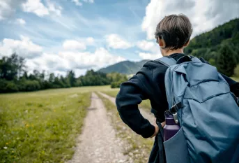 Garçon adolescent, de dos, face à un chemin en randonnée, avec son sac à dos.